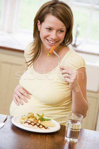 Mulher grávida cozinha alimentação frango legumes sorridente Foto stock © monkey_business