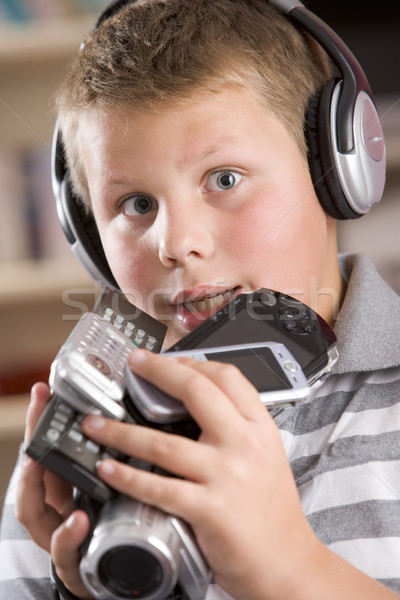 Stock photo: Young boy wearing headphones in bedroom holding many electronic 