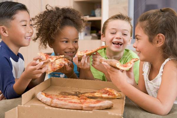 Stock photo: Four young children indoors eating pizza smiling