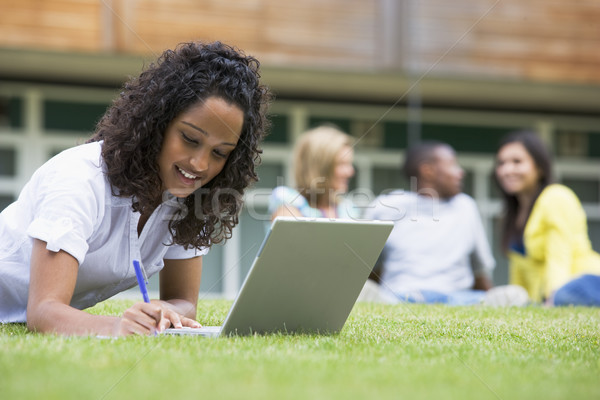 Young woman using laptop on campus lawn, with other students rel Stock photo © monkey_business