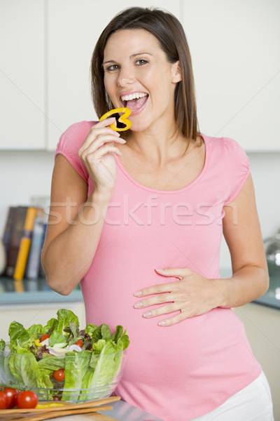 Stock photo: Pregnant woman in kitchen making a salad and smiling