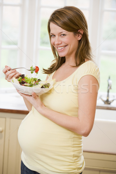 Stock photo: Pregnant woman in kitchen eating a salad smiling