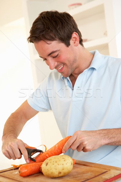 Stock photo: Happy young man peeling vegetable in kitchen