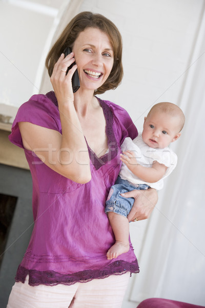 Mother in living room using telephone holding baby smiling Stock photo © monkey_business