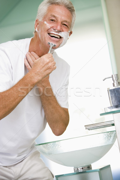 Man in bathroom shaving and smiling Stock photo © monkey_business