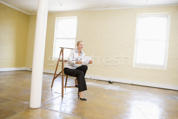 Woman sitting on ladder in empty space holding paper smiling Stock photo © monkey_business