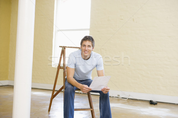 Man sitting on ladder in empty space holding paper smiling Stock photo © monkey_business