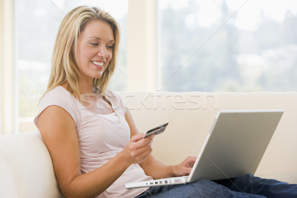 Stock photo: Woman in living room using laptop and holding credit card smilin