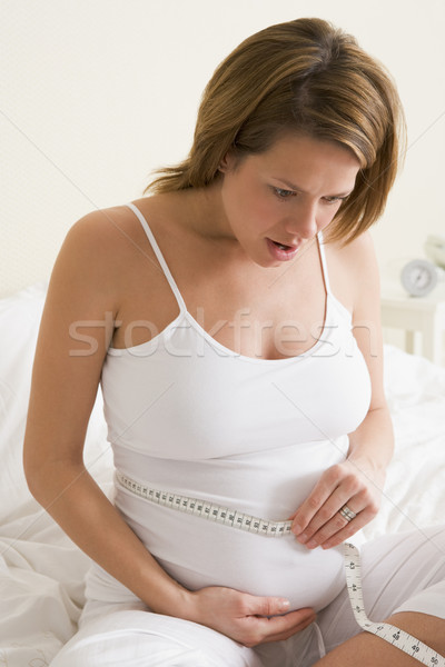 Pregnant woman in bedroom measuring belly looking worried Stock photo © monkey_business