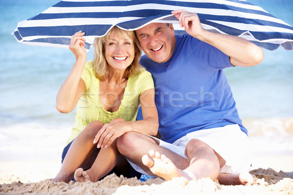 Senior Couple Sheltering From Sun Under Beach Umbrella Stock photo © monkey_business