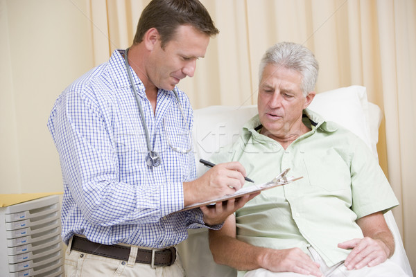 Doctor writing on clipboard while giving man checkup in exam roo Stock photo © monkey_business