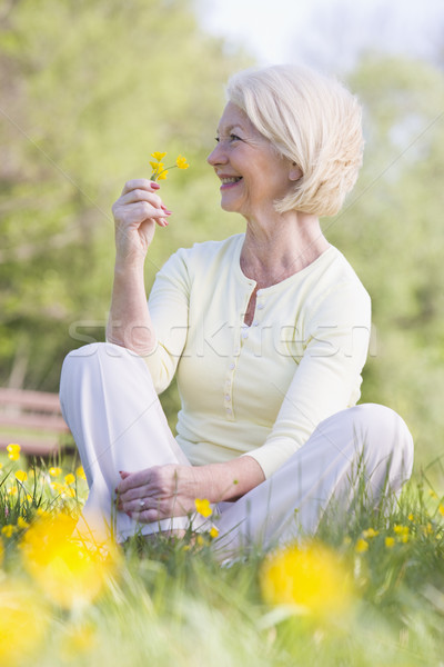 Woman sitting outdoors smiling and holding a Buttercup flower Stock photo © monkey_business
