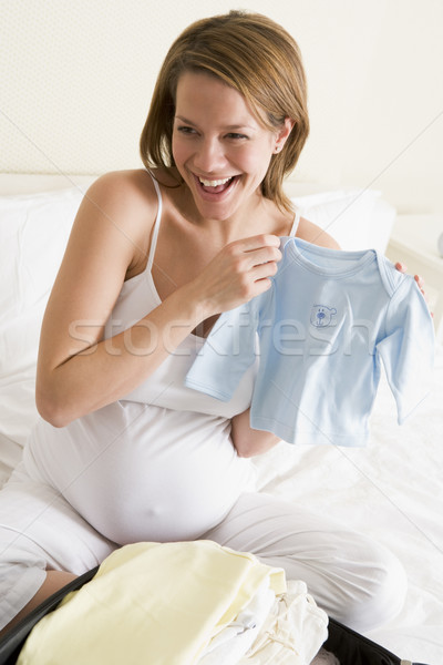 Stock photo: Pregnant woman packing baby clothing in suitcase smiling