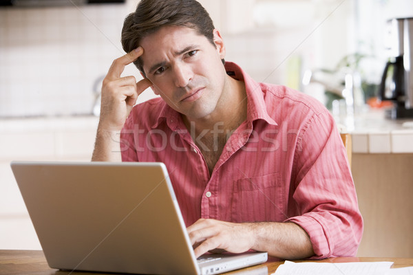 Man in kitchen using laptop frowning Stock photo © monkey_business