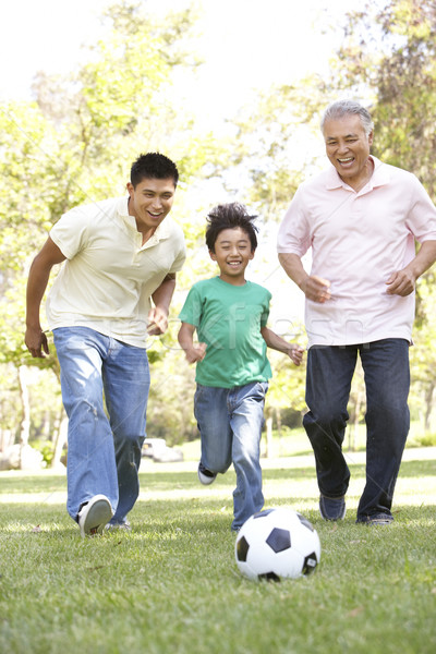 Grandfather With Son And Grandson Playing Football In Park Stock