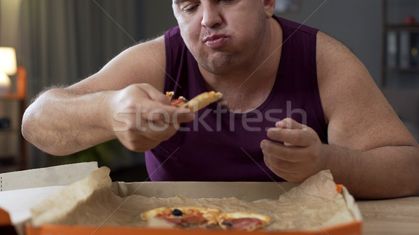Overweight male eating pizza with delight at night, addiction to unhealthy food Stock photo © motortion