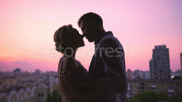 Couple in love gently kissing, standing on roof of house, beautiful sunset Stock photo © motortion