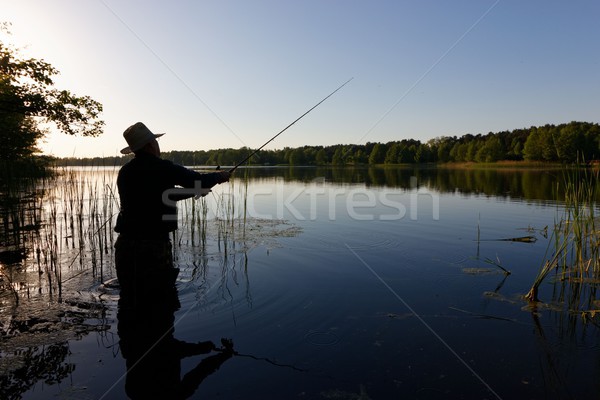 Pescatore silhouette piedi lago pesce Foto d'archivio © mtmmarek