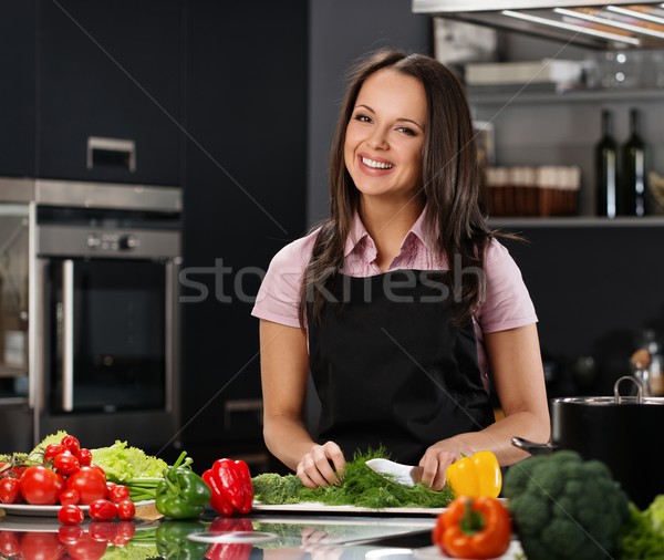 Happy young woman in apron on modern kitchen cutting vegetables Stock photo © Nejron