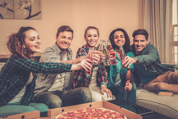 Stock photo: Group of young multi-ethnic friends with pizza and bottles of drink celebrating in home interior