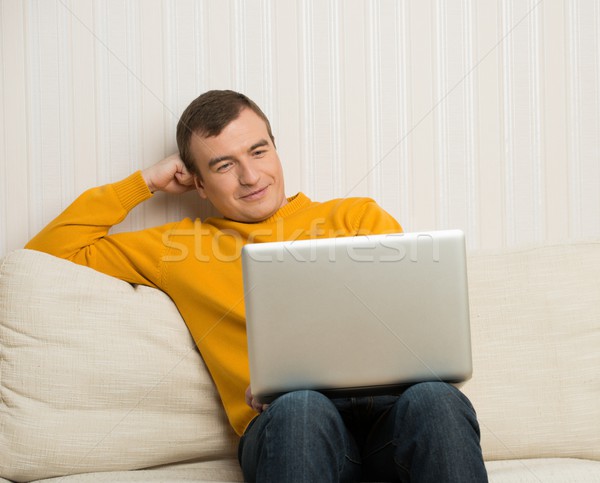 Handsome young man in yellow pullover with laptop in home interior Stock photo © Nejron