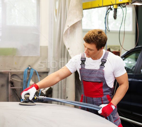 Young serviceman performing grinding with machine on a car bonnet in a workshop Stock photo © Nejron