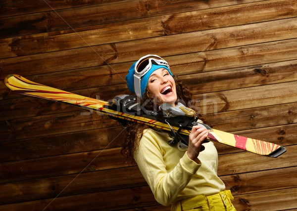 Stock photo: Smiling woman with skies standing against wooden house wall 