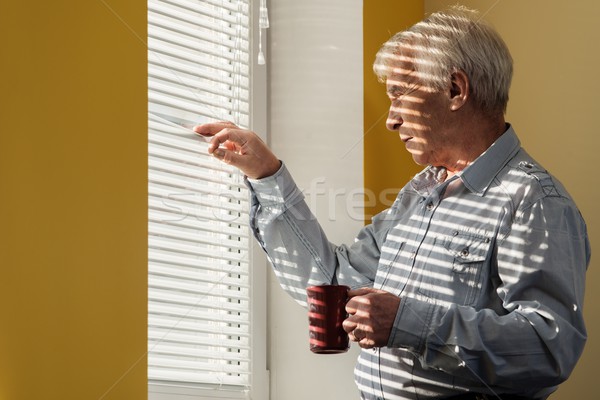 Senior man with cup looking out the window through jalousie  Stock photo © Nejron