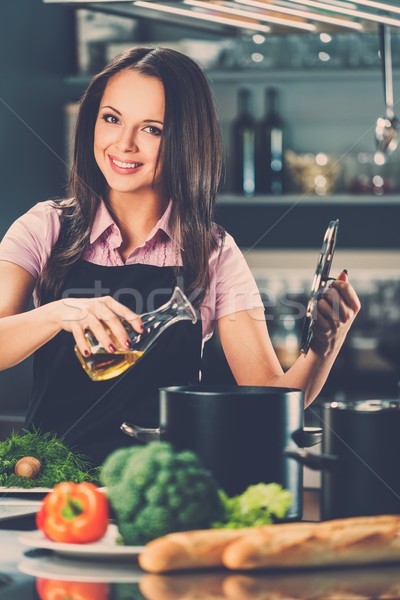 Smiling young woman adding oil to pot on a modern kitchen  Stock photo © Nejron