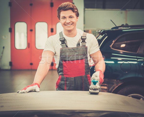 Young serviceman performing grinding with machine on a car bonnet in a workshop Stock photo © Nejron