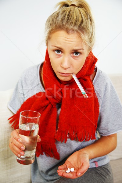 Sick young blond woman with pills, thermometer, and glass of water Stock photo © Nejron