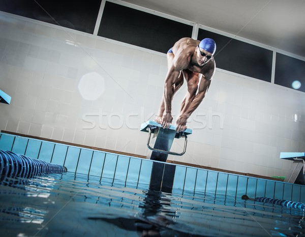 Young muscular swimmer in low position on starting block in a swimming pool Stock photo © Nejron