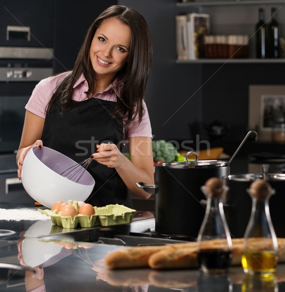 Young woman in apron whisking eggs for a dough on a modern kitchen Stock photo © Nejron