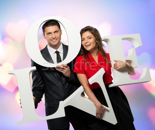 Stock photo: Beautiful smiling couple holding word LOVE over bokeh background 