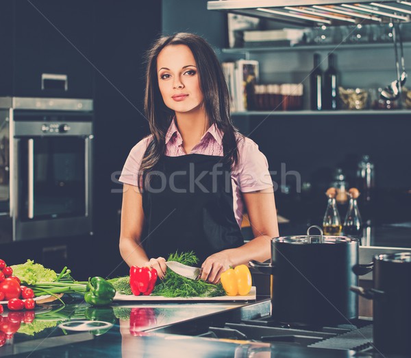 Cheerful young woman in apron on modern kitchen cutting vegetables Stock photo © Nejron