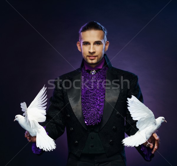 Young handsome brunette magician man in stage costume with his trained white doves Stock photo © Nejron