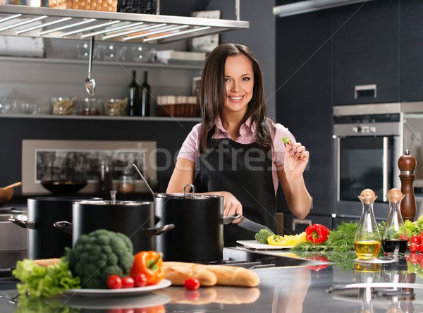 Cheerful young woman in apron on modern kitchen cutting vegetables Stock photo © Nejron