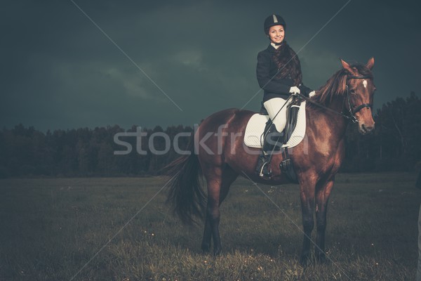 Beautiful girl sitting on a horse outdoors against moody sky Stock photo © Nejron