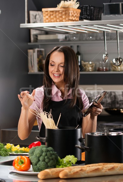 Stock photo: Smiling young woman cooking spaghetti on a modern kitchen 