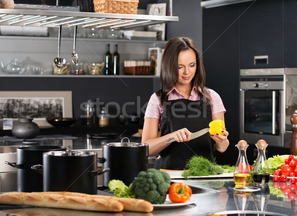 Cheerful young woman in apron on modern kitchen cutting vegetables Stock photo © Nejron