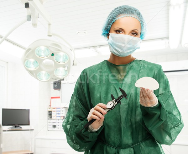 Plastic surgeon woman with silicon breast implant and calliper in surgery room interior  Stock photo © Nejron