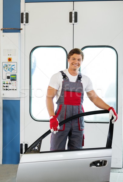 Cheerful serviceman with car door near paint booth in a car body workshop Stock photo © Nejron