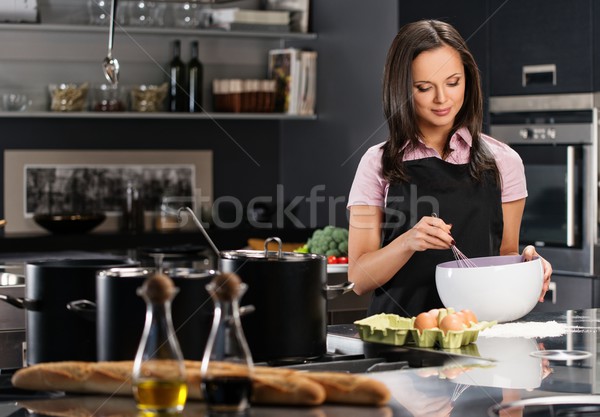 Young woman in apron whisking eggs for a dough on a modern kitchen Stock photo © Nejron