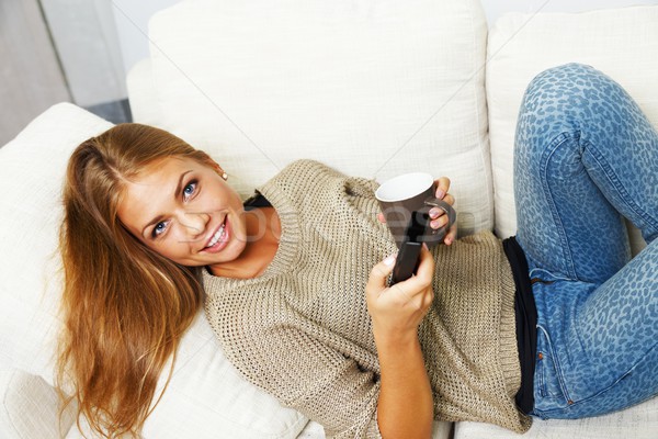 Young beautiful woman on a sofa with remote control and mug Stock photo © Nejron