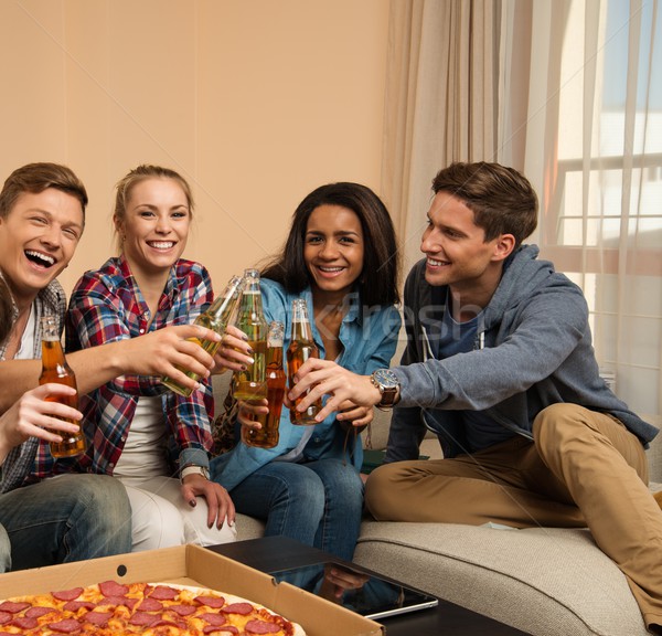 Group of young friends with pizza and bottles of drink celebrating in home interior Stock photo © Nejron