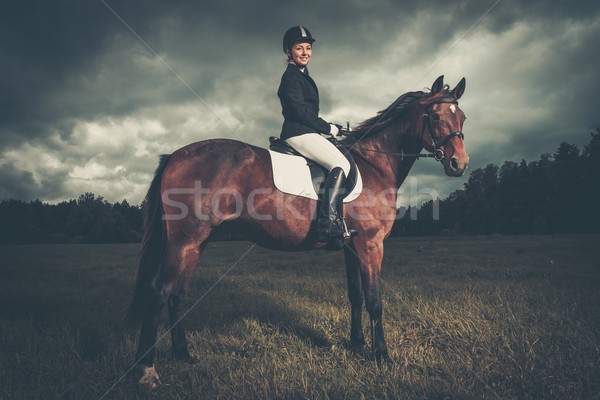 Beautiful girl sitting on a horse outdoors against moody sky Stock photo © Nejron