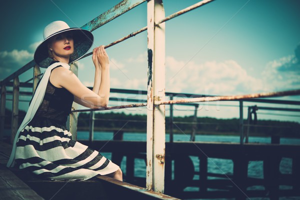 Beautiful woman wearing hat and white scarf sitting on old wooden pier  Stock photo © Nejron