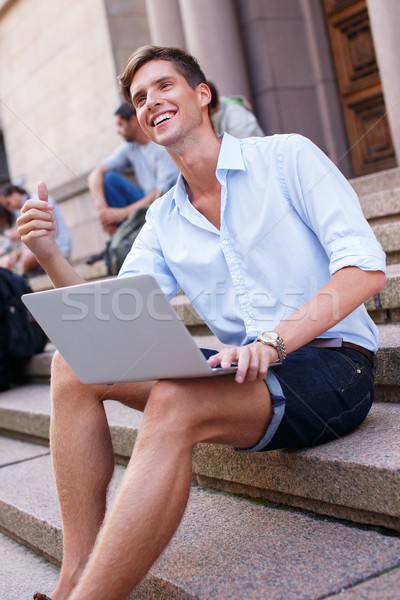 Stock photo: Handsome young man with laptop sitting on a steps outdoors