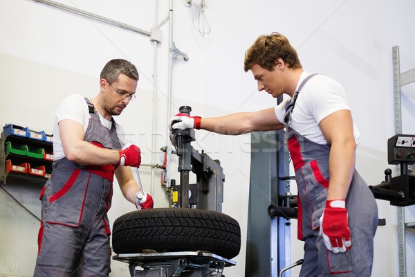 Two mechanics changing tire on a wheel in a car workshop Stock photo © Nejron