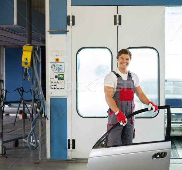 Cheerful serviceman with car door near paint booth in a car body workshop Stock photo © Nejron